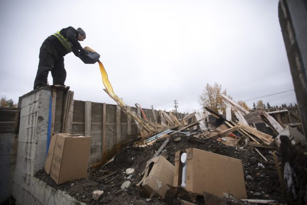 Kurtus Dennis, Iyon Kechika firesmarting crew member, pours oil on the former residential school in Lower Post, B.C., before it was set on Sep 29, 2021.