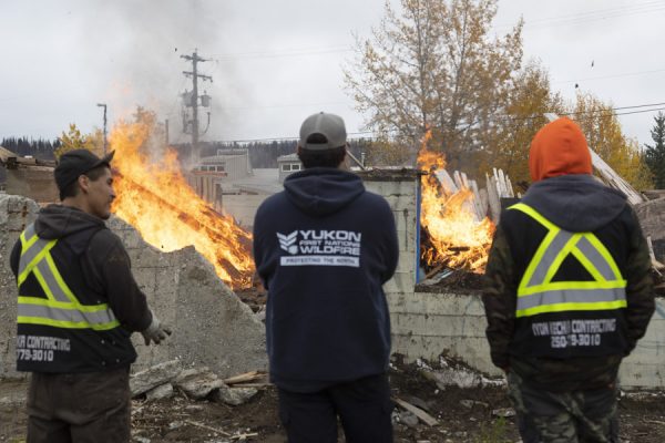 Firesmart and wild land fire fighting crew members watch as the remains of the former residential school in Lower Post, B.C., burn on Sep 29, 2021.