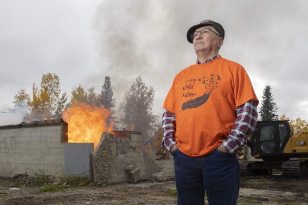 Lower Post, B.C., residential school survivor Melvin Tibbett poses for a photo as the former school burns behind him on Sep 29, 2021.